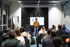 A speaker presenting to a seated audience at an Experience Cafe meetup